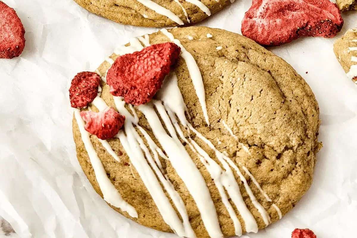 A cookie on a white surface, drizzled with white icing and topped with pieces of dried strawberries—a Valentine's dessert idea that is sure to wow your sweetheart.