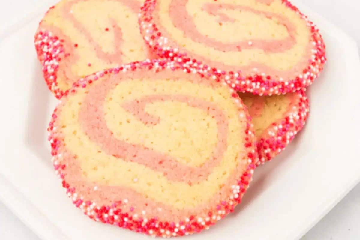 Swirled pink and vanilla cookies with red, pink, and white sprinkles on the edges, arranged on a white plate—perfect Valentine dessert ideas to wow your sweetheart.