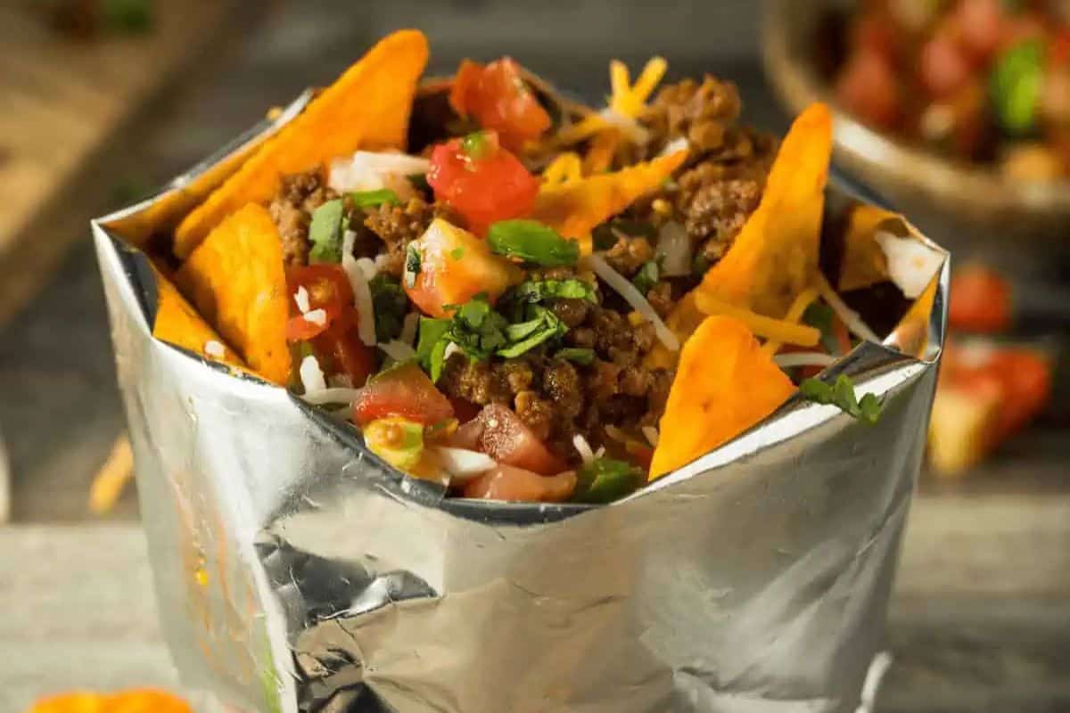 A walking taco in a foil bag, featuring Doritos, ground beef, shredded cheese, diced tomatoes, and cilantro—perfect as a touchdown treat for your game day party.