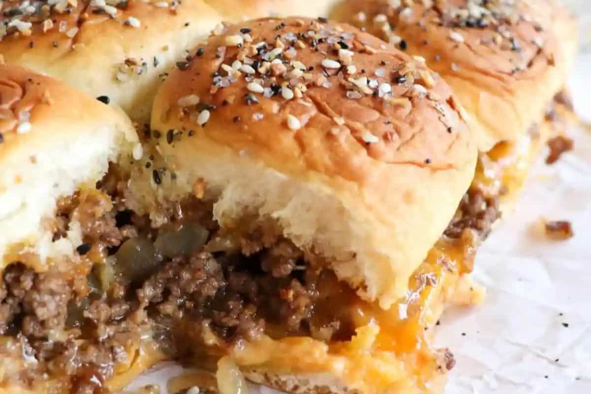 Close-up of irresistible hamburger sliders with ground beef, melted cheese, and onions, topped with sesame seeds on soft buns. Perfect for game day indulgence.