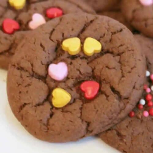 Chocolate cookies topped with heart-shaped and round sprinkles on a white plate make for delightful Valentine dessert ideas to wow your sweetheart.
