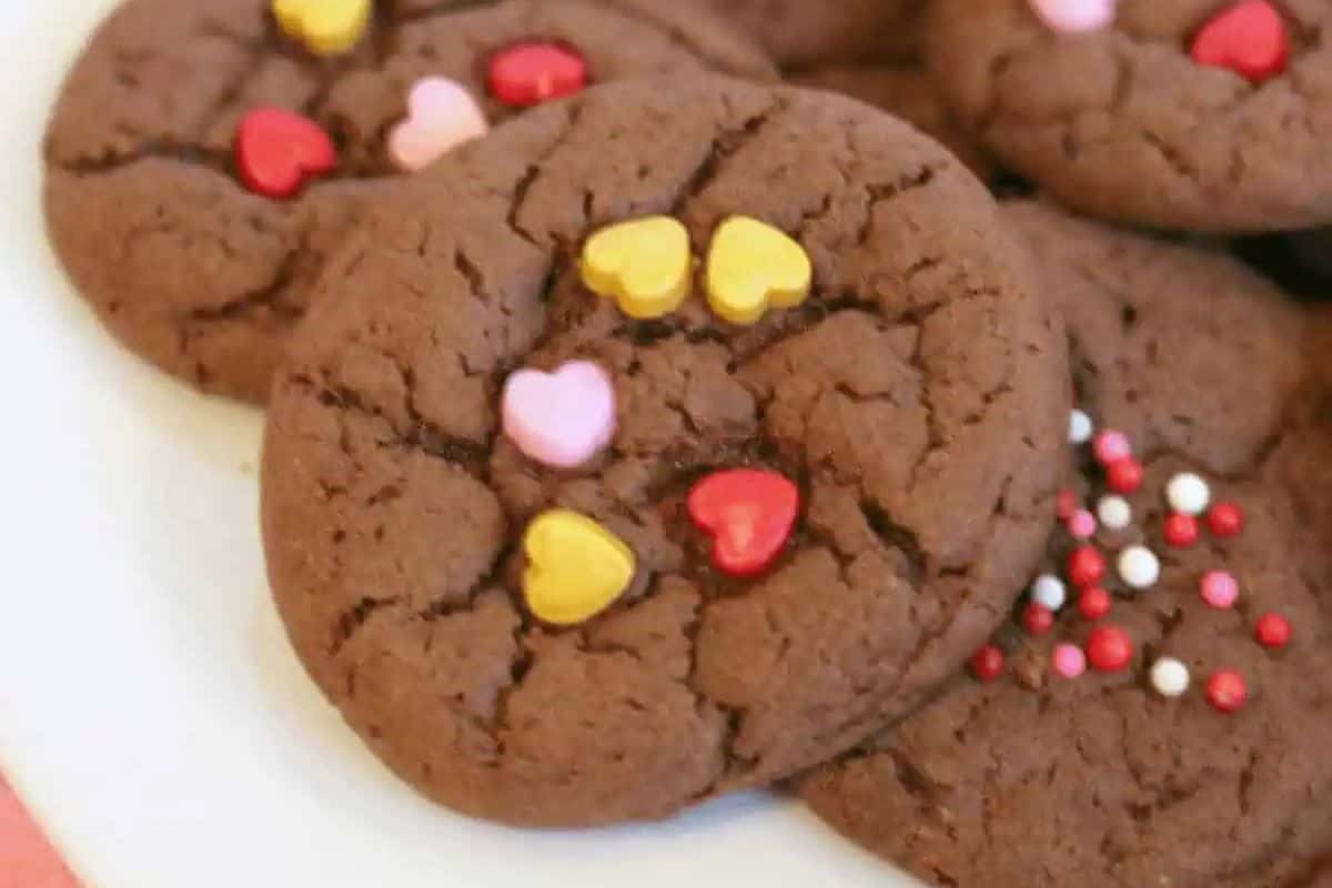 Chocolate cookies topped with heart-shaped and round sprinkles on a white plate make for delightful Valentine dessert ideas to wow your sweetheart.