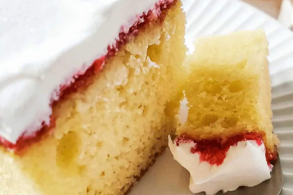 A slice of sponge cake with white frosting and a red layer in between, served on a white plate—perfect for wow-ing your sweetheart this Valentine’s Day.