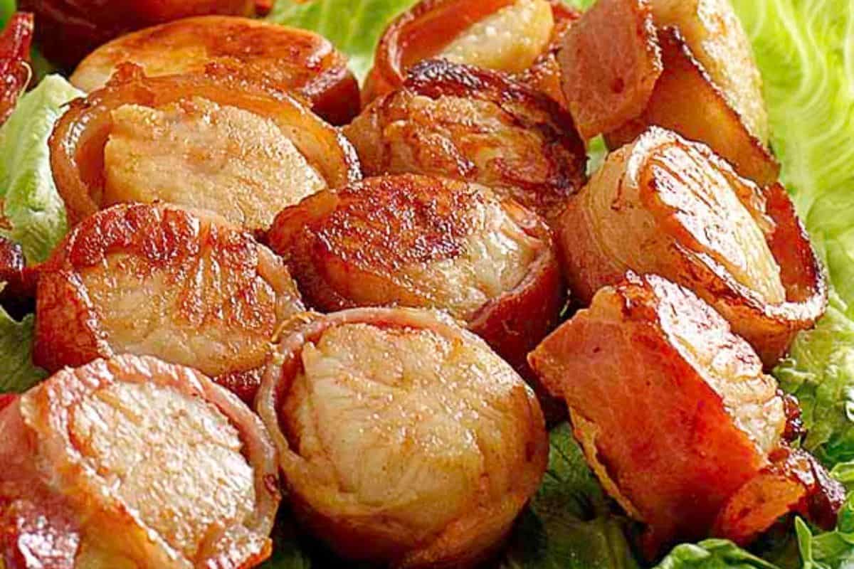 Close-up of cooked scallops wrapped in crispy bacon, served on a bed of green lettuce leaves—a Red Lobster copycat recipe you can easily make at home.
