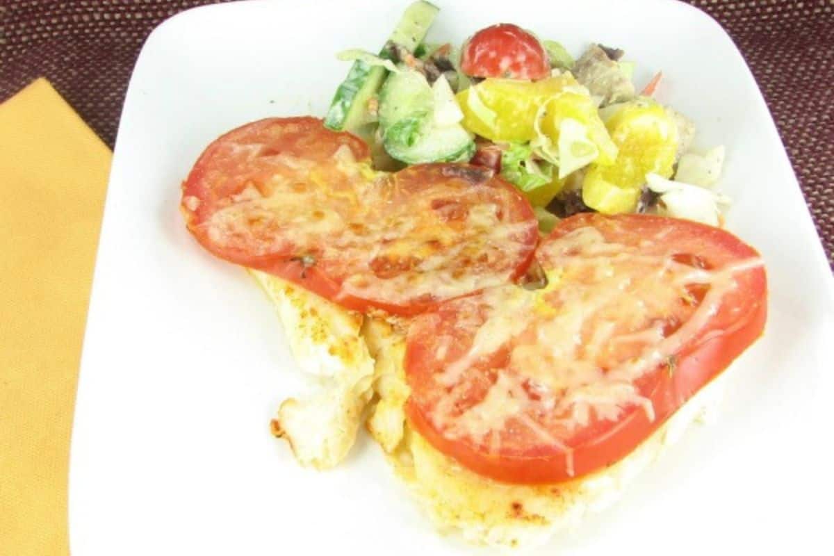 A plate with sliced baked tomatoes topped with melted cheese, served alongside a mixed vegetable salad—perfect for making at home with easy copycat recipes.