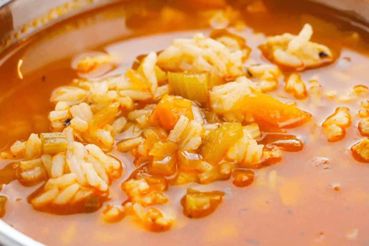 A close-up of a bowl of tomato-based soup with rice, diced carrots, and celery in a clear broth—one of those comforting soups sure to warm your soul.