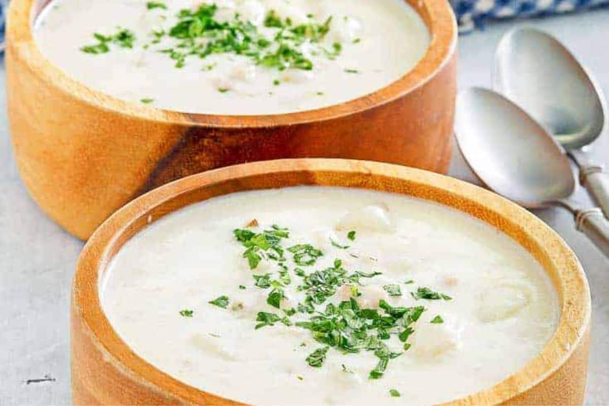 Two wooden bowls filled with creamy soup, garnished with chopped herbs, are placed next to two metal spoons—perfect for trying your favorite Red Lobster copycat recipes at home.