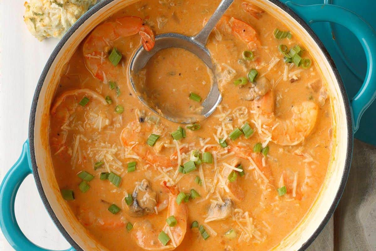 A pot of creamy seafood soup with shrimp, mushrooms, shredded cheese, and chopped green onions, with a ladle resting inside—a comforting dish you can make at home inspired by Red Lobster copycat recipes.