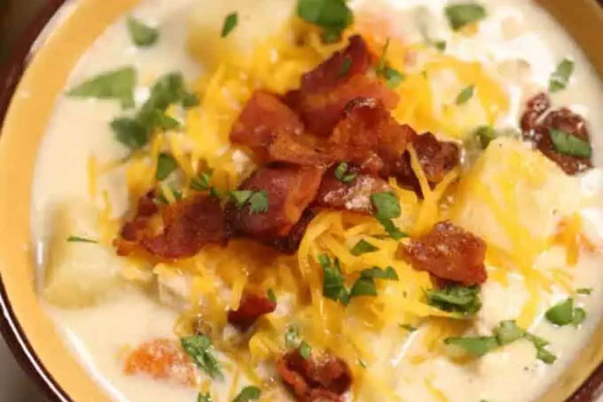 A bowl of creamy soup to warm your soul, topped with shredded cheese, crispy bacon pieces, and chopped fresh herbs.