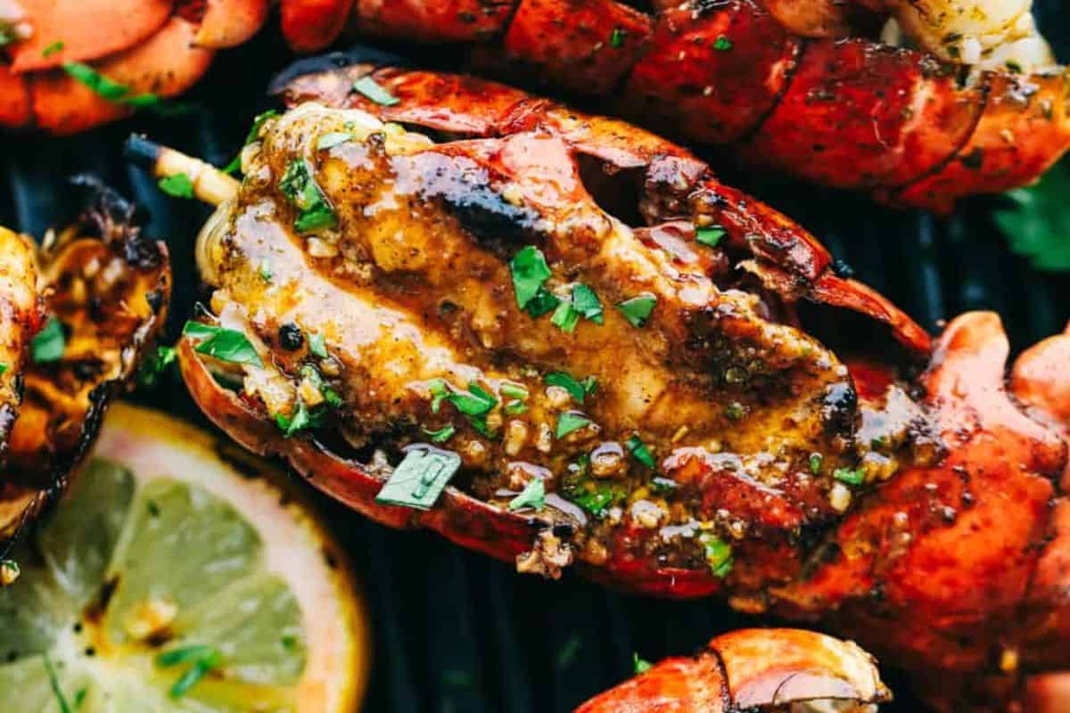 Close-up of a grilled lobster tail topped with herbs and spices, garnished with a slice of lemon in the background—perfect for cozy nights or as the highlight of special dinners.