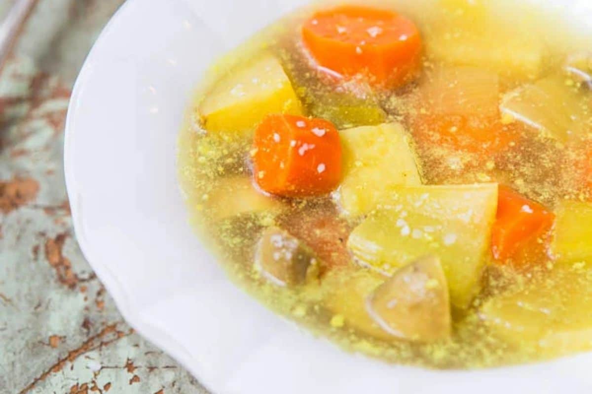 A close-up of a bowl of cozy vegetable soup featuring carrots, potatoes, and broth on a white plate—perfect to warm up on chilly days.