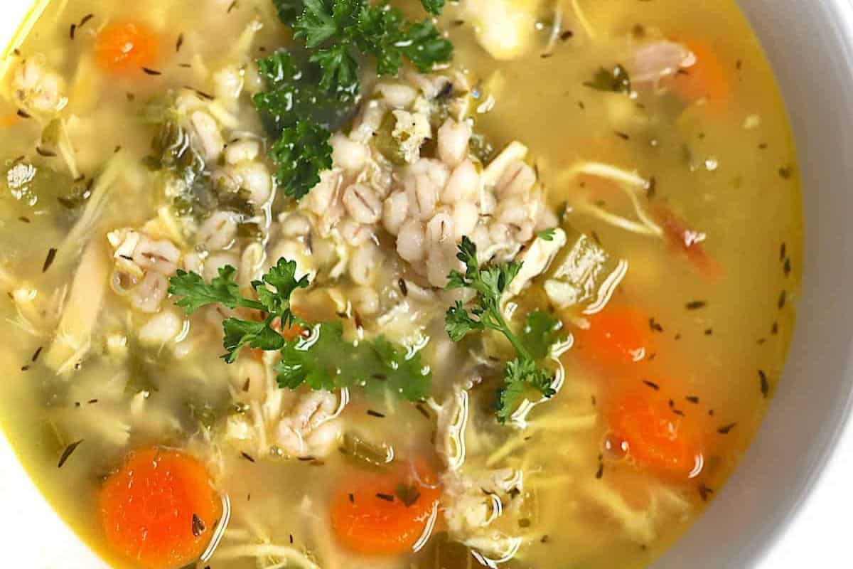 A bowl of chicken barley soup with carrots, herbs, and parsley garnish in a clear broth—one of those comforting soups sure to warm your soul.