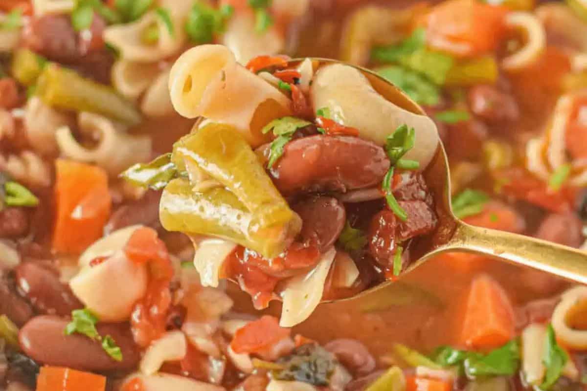 A spoonful of minestrone soup with pasta, green beans, kidney beans, carrots, tomatoes, and herbs—a classic pasta soup perfect for family friendly meals.