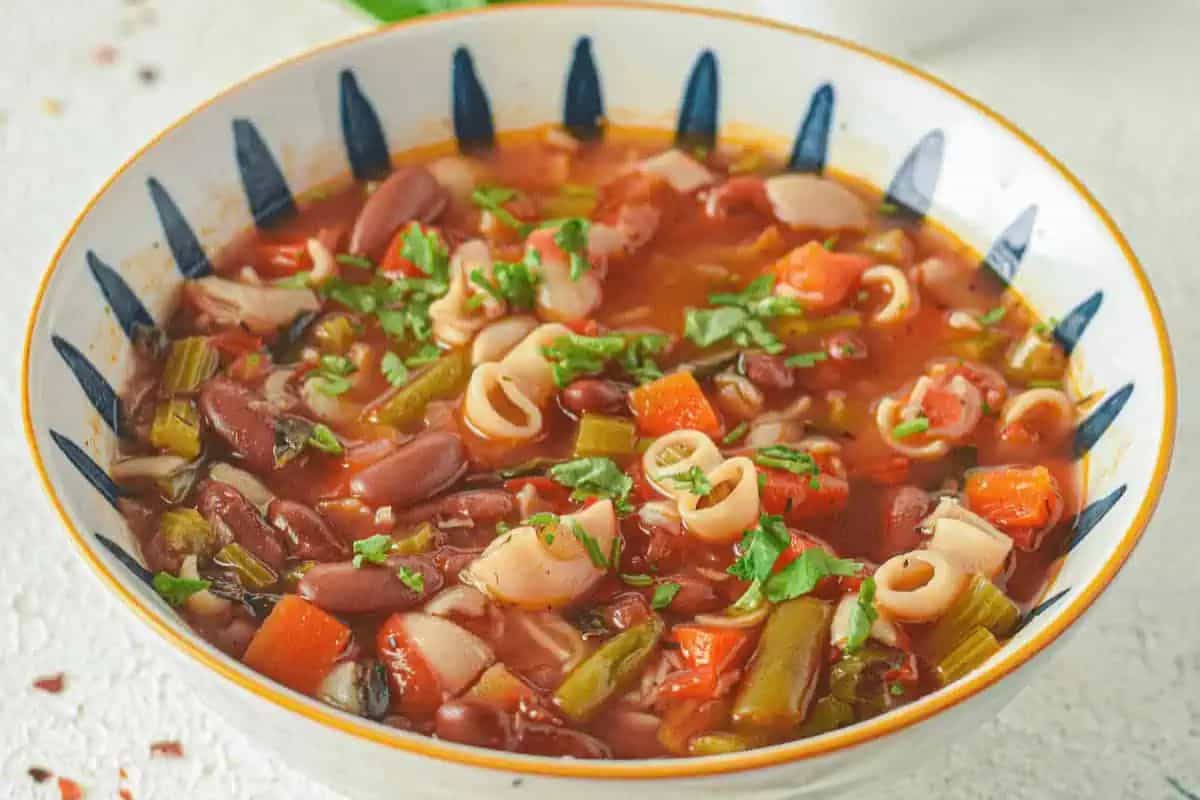A bowl of minestrone soup with pasta, kidney beans, chopped vegetables, and herbs in a tomato-based broth—one of the coziest vegetable soups to warm up with.