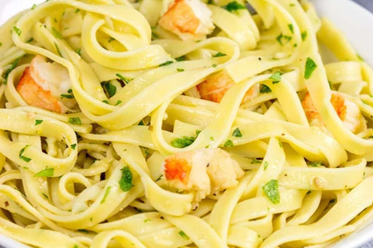 A plate of fettuccine pasta with pieces of lobster and chopped parsley, lightly coated in a sauce—perfect for special dinners or when you’re searching for exceptional lobster recipes.