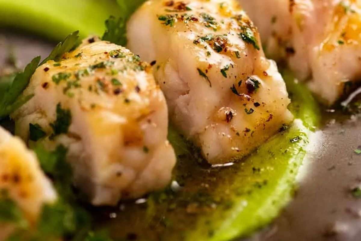 Close-up of seared pieces of white fish garnished with herbs, served on a green vegetable puree with a light sauce—perfect for special dinners and cozy nights in.