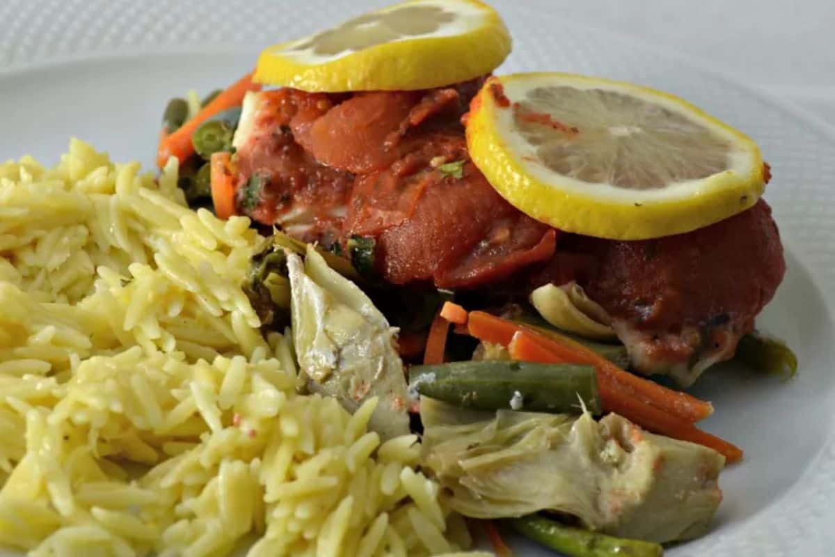 A plate of yellow rice with a vegetable medley, topped with two pieces of fish covered in tomato sauce and garnished with lemon slices—perfect to make at home for fans of Red Lobster copycat recipes.