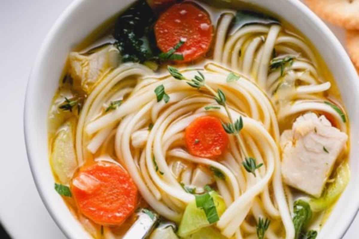 A bowl of chicken soup with sliced carrots, leafy greens, herbs, and chunks of chicken in a clear broth—one of those comforting soups sure to warm your soul.