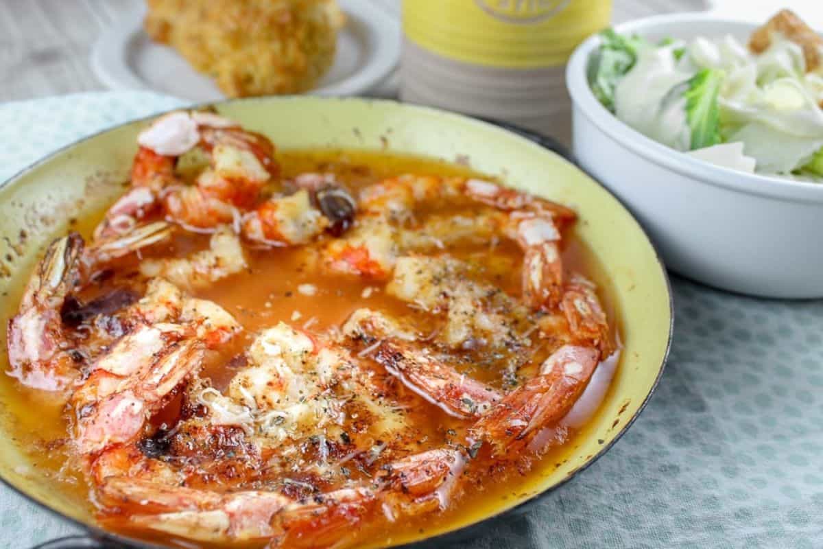 A pan of cooked shrimp in a seasoned sauce, inspired by Red Lobster, served alongside a bowl of salad and a biscuit on a plate in the background.
