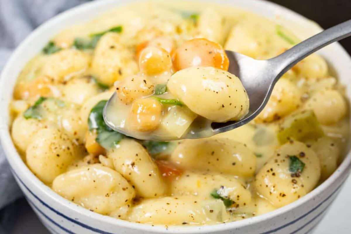 A close-up of a spoonful of creamy gnocchi soup with vegetables and herbs, served in a white bowl—a cozy addition to your collection of family friendly soups.