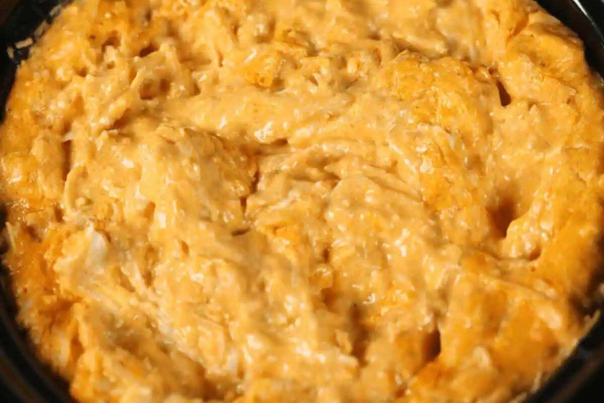 Close-up of a creamy, orange-colored dip with a textured surface, likely made with cheese and shredded chicken, in a black dish—perfect for fans of easy Slow Cooker Dips.