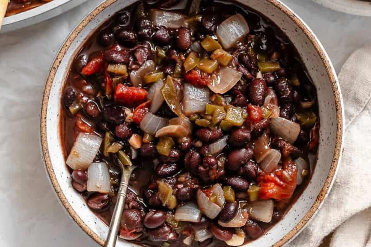 A bowl of black bean soup with chopped onions, tomatoes, and green peppers, with a spoon inside—a must try for fans of chili recipes.
