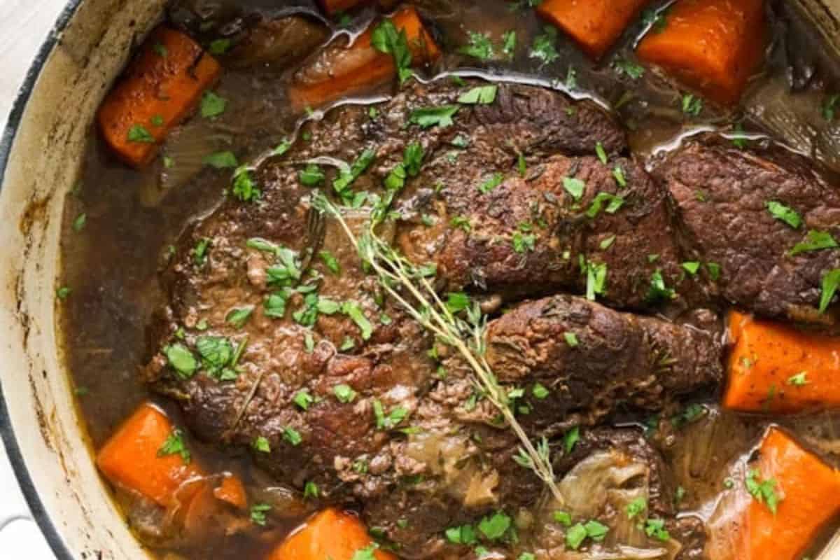 A family friendly cooked pot roast with carrots, fresh herbs, and brown gravy in a large pot—perfect for easy dinner nights and those looking for classic chuck roast recipes.