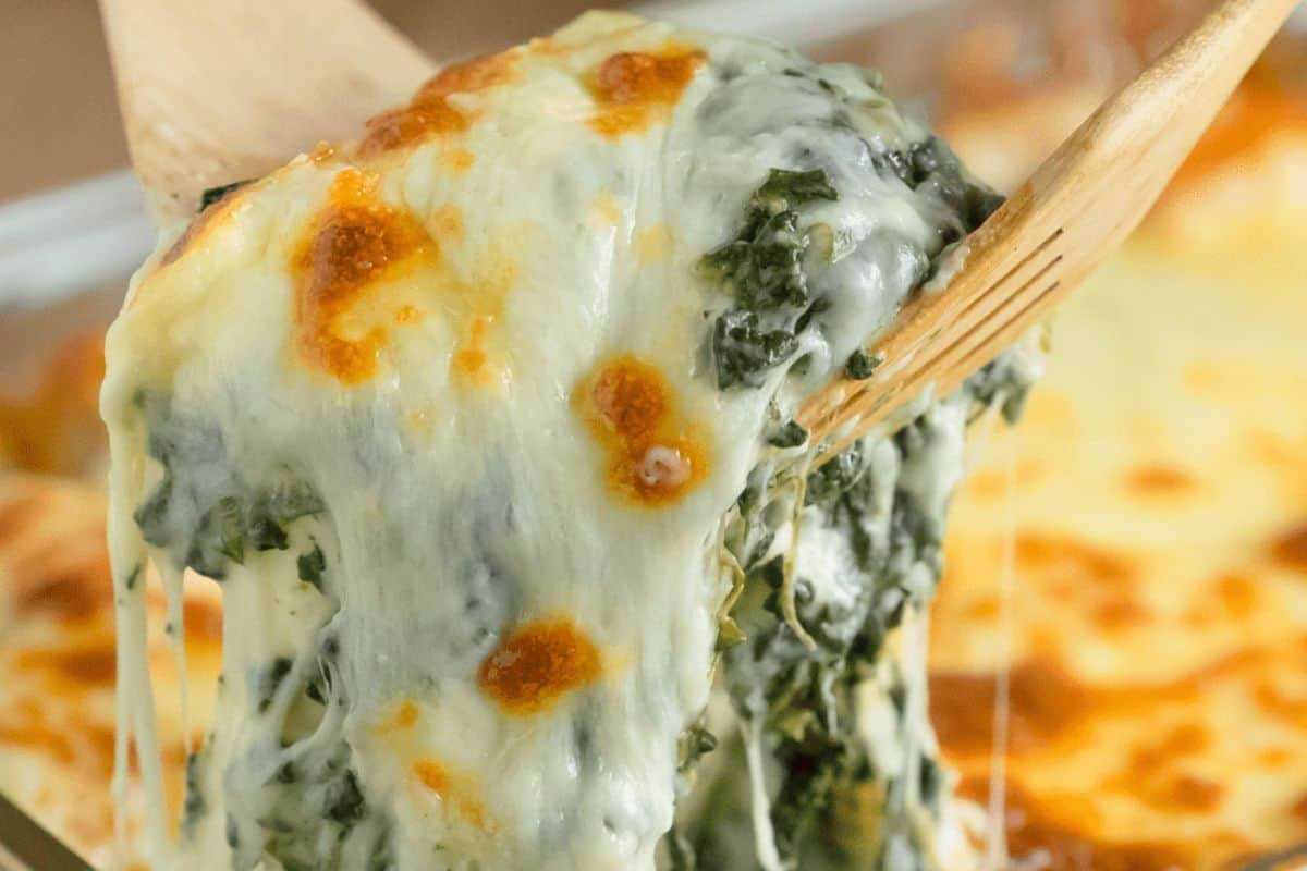 A close-up of a serving of baked spinach lasagna being lifted, with melted cheese stretching from the pan—perfect alongside your favorite Slow Cooker Dips for a cozy gathering.