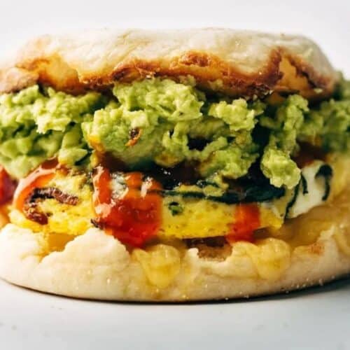 English muffin sandwich filled with egg, melted cheese, mashed avocado, and drizzled with hot sauce—one of our favorite easy Weight Watchers recipes—served on a white background.