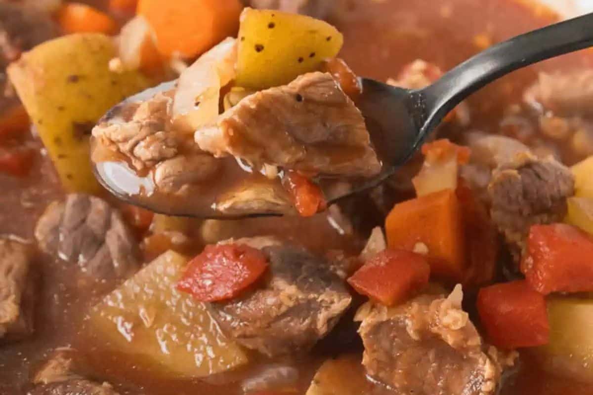 A close-up of a spoonful of beef stew with chunks of beef, potatoes, carrots, and tomatoes in broth—a family friendly favorite that everyone loves, perfect for anyone searching for delicious chuck roast recipes.
