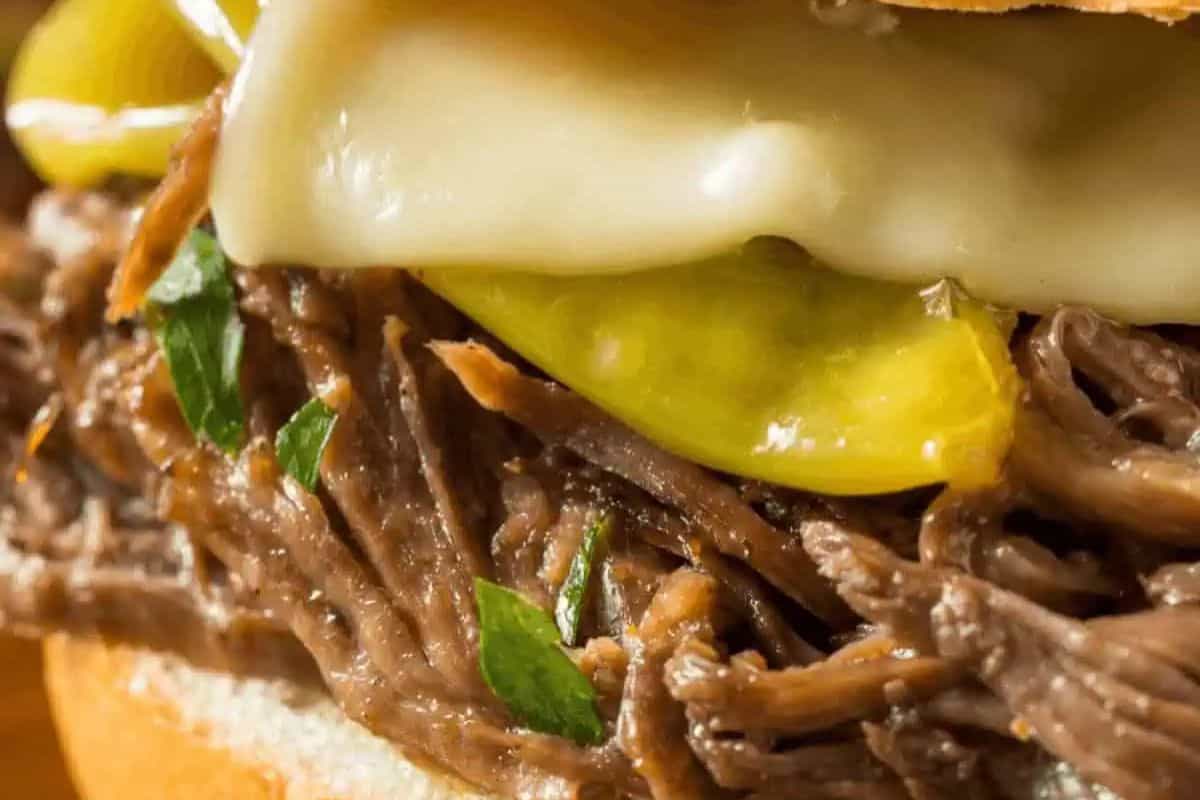 Close-up of a sandwich with shredded beef, melted cheese, sliced pepperoncini, and chopped herbs on a bun—perfect for easy dinner nights and a family friendly twist on classic chuck roast recipes.
