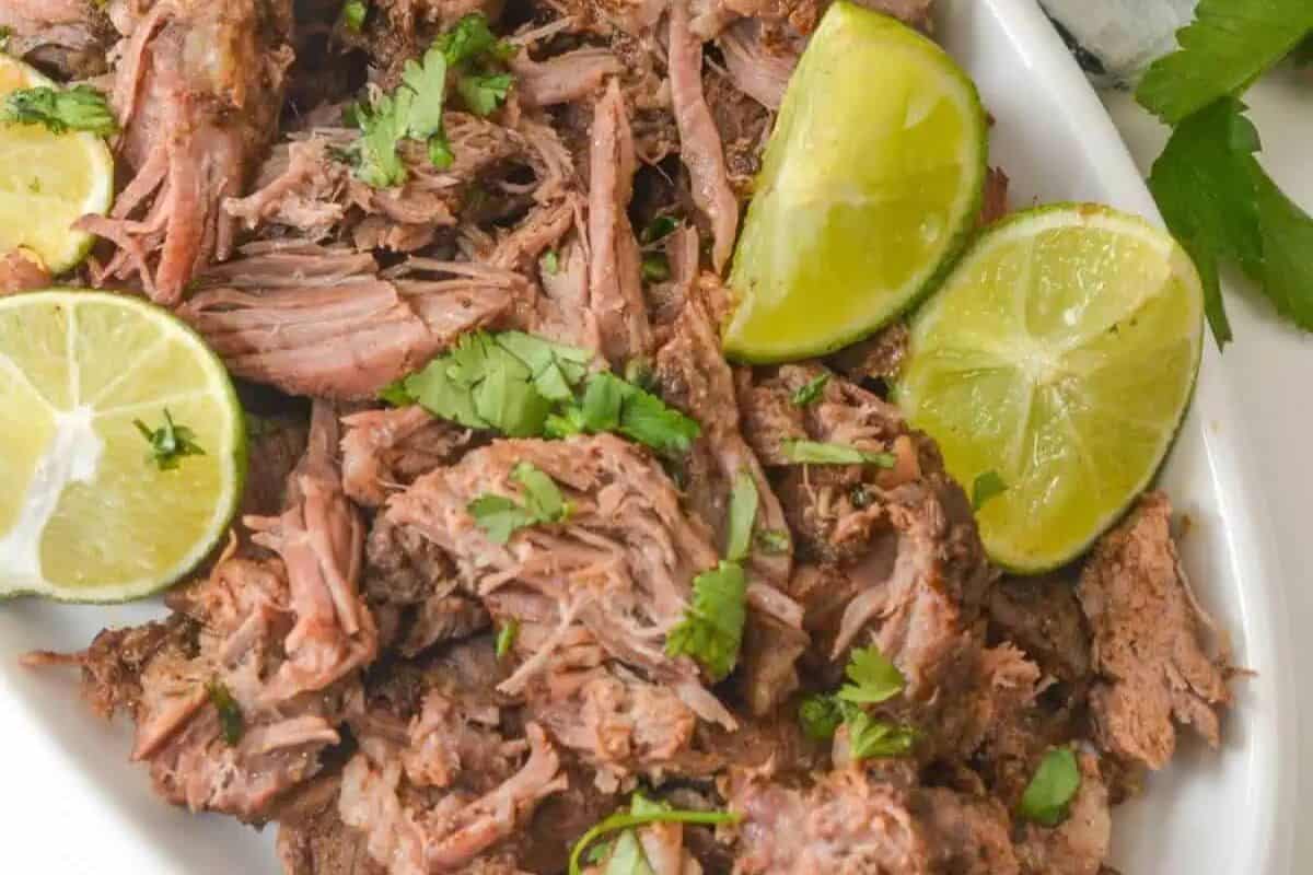 Shredded cooked meat garnished with chopped cilantro and served with lime wedges on a white plate—an everyone loves classic perfect for family friendly Chuck roast recipes.