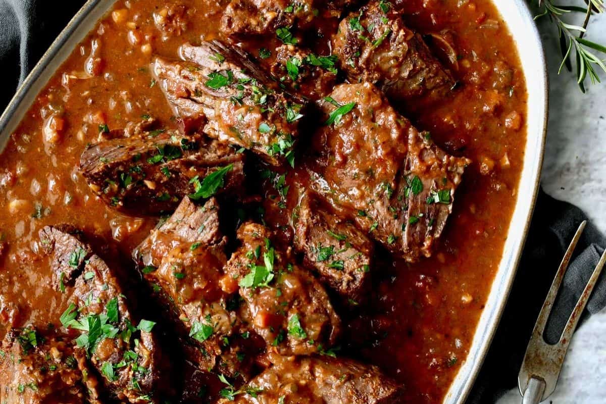 Chunks of braised beef in a thick tomato-based sauce, garnished with chopped parsley, served in an oval dish—a family friendly option that's perfect for easy dinner nights.