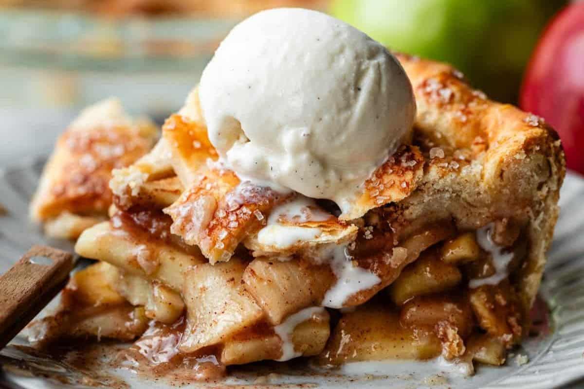 Close-up of a slice of apple pie, served on a blue plate and topped with a scoop of vanilla ice cream.