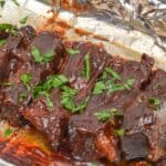 Several pieces of glazed, cooked meat garnished with chopped parsley on a foil-lined baking tray.