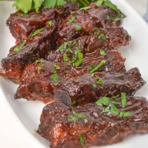 Barbecue-glazed Baked Country Style Ribs garnished with chopped fresh parsley, served on a white plate.