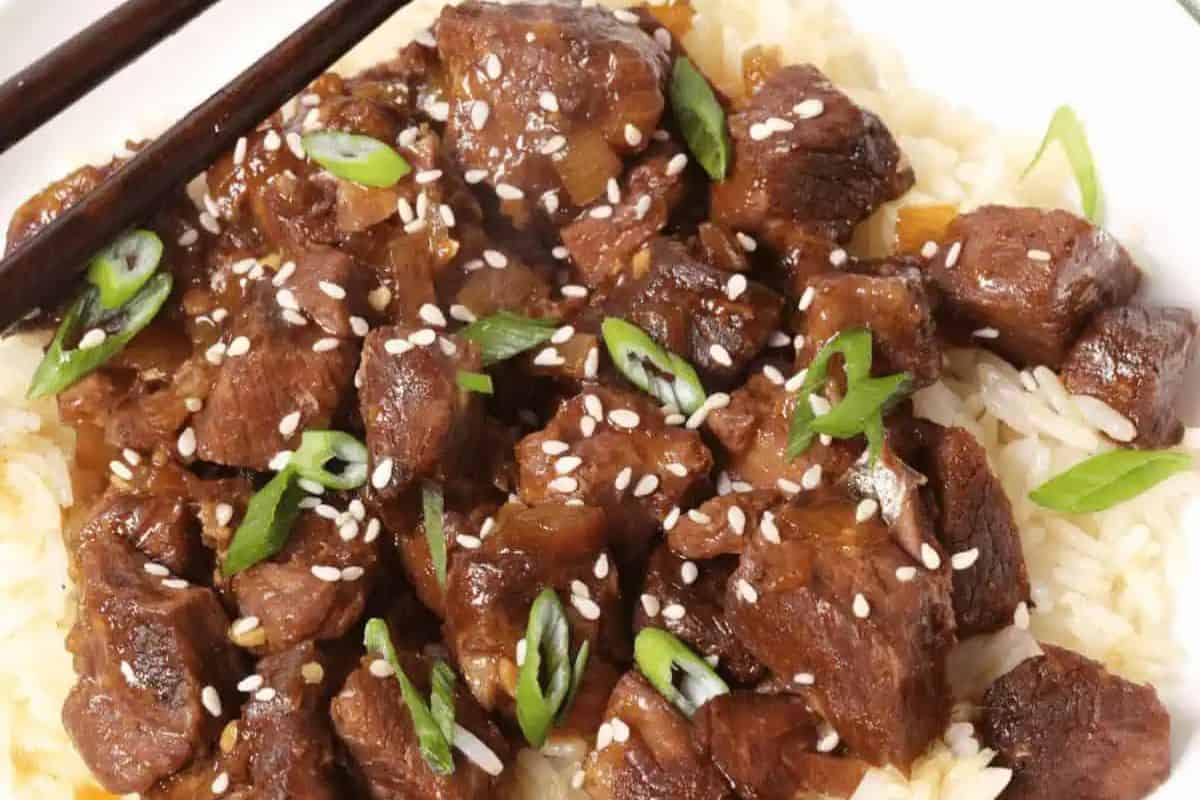 A plate of beef stew served over white rice, topped with sliced green onions and sesame seeds, with chopsticks on the side—perfect for easy dinner nights or those searching for comforting slow cooker recipes.