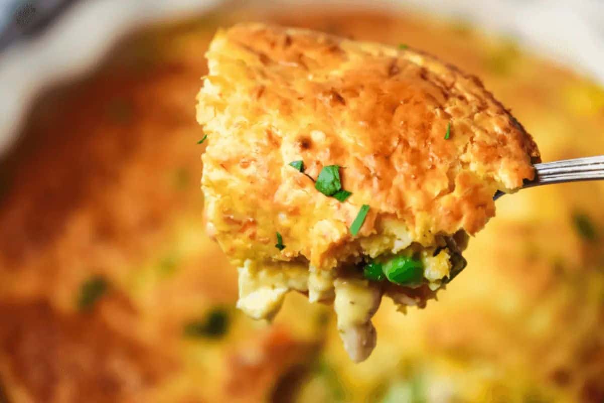 Close-up of some chicken pot pie with a golden crust, served on a silver spoon.