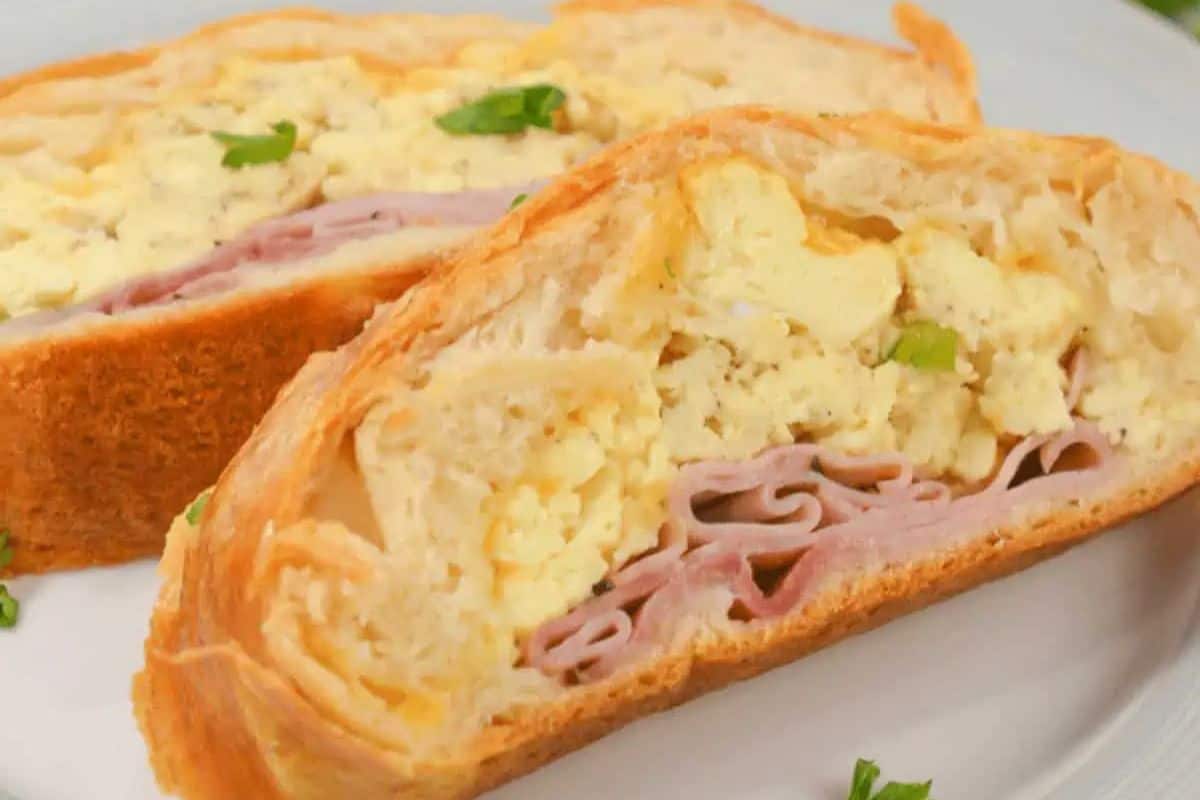 Slices of a baked pastry filled with scrambled eggs and ham, garnished with parsley, make for a delightful breakfast on a white plate.