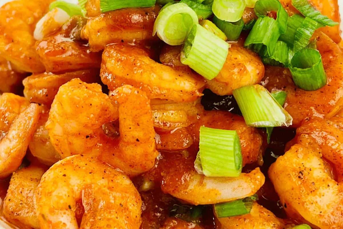 Close-up of buffalo shrimp topped with chopped green onions. The shrimp are coated in a reddish sauce, giving it a restaurant-quality allure. The dish appears fresh and seasoned to perfection, making it one of those easy recipes you'll want to recreate at home.