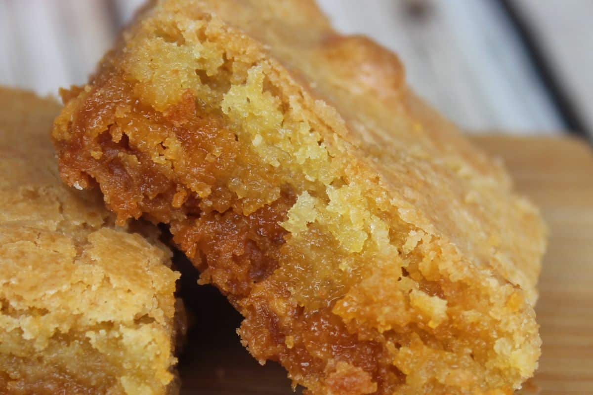 Close-up of two moist butterscotch blondies with a golden-brown crust, showcasing a soft, chewy texture reminiscent of brownies on a wooden surface.