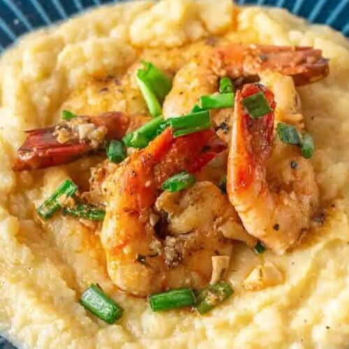 Enjoy a restaurant-quality experience with shrimp and chopped green onions nestled on a bed of creamy grits, elegantly served on a blue plate.