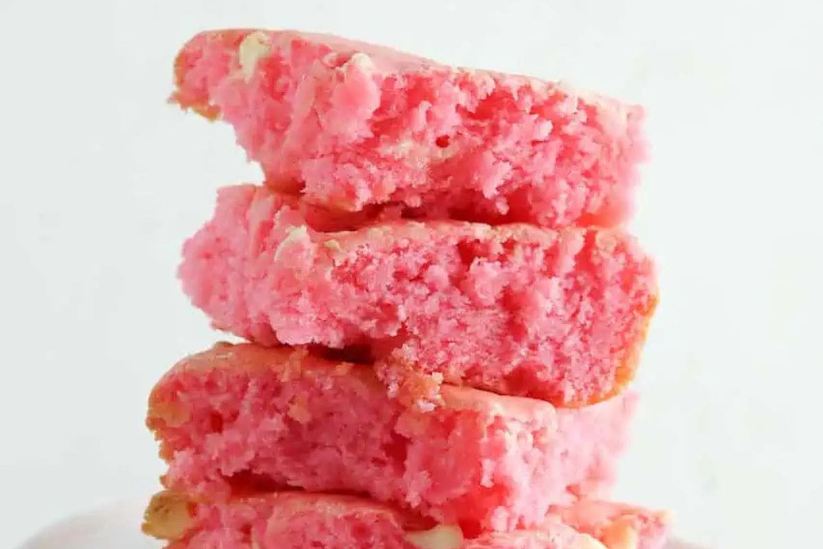A stack of four bright pink strawberry brownies with a crumbly texture on a white background.