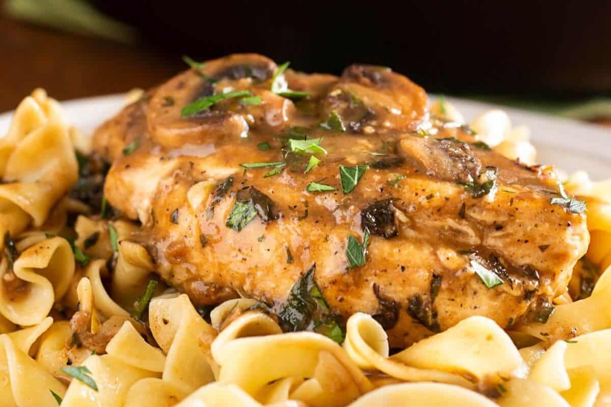 A plate of Chicken Marsala with a creamy mushroom sauce over egg noodles, garnished with parsley.