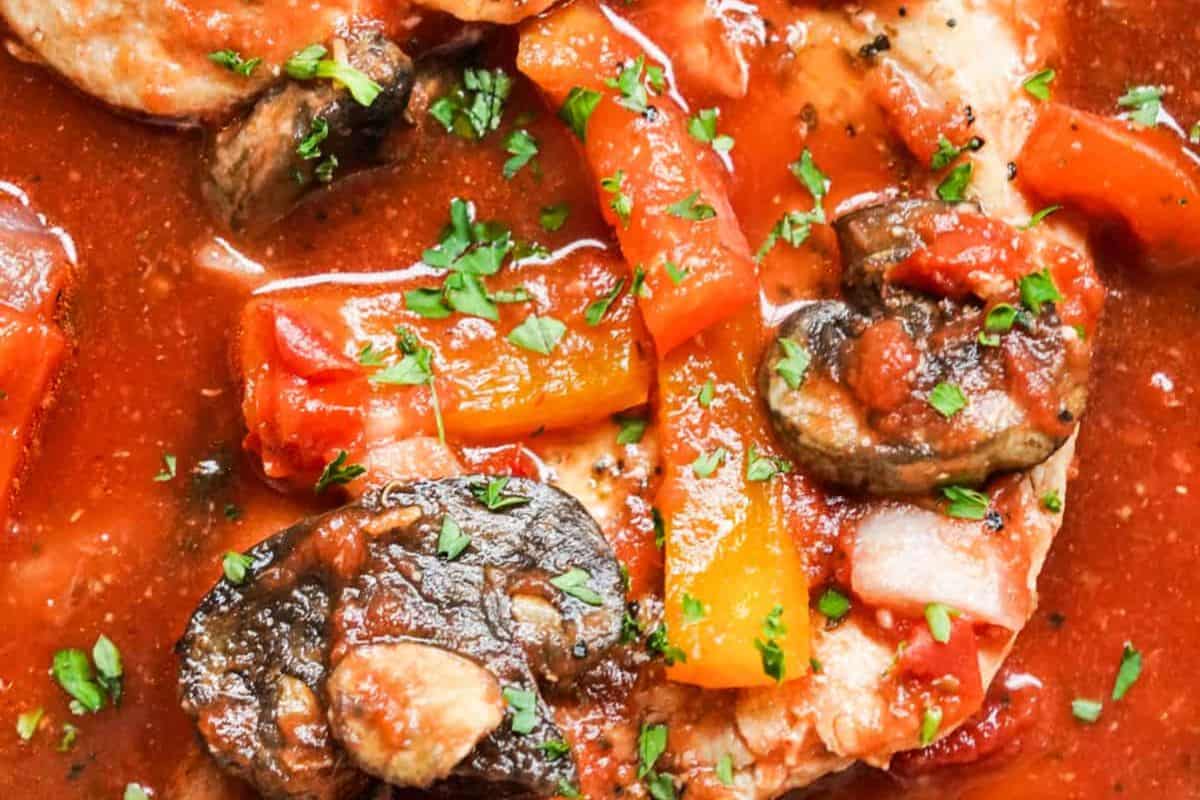 Close-up of a cooked dish featuring pork, sliced mushrooms, bell peppers, and tomato sauce, garnished with chopped parsley—perfect inspiration for your dinner routine or to add to your favorite dinner recipes.