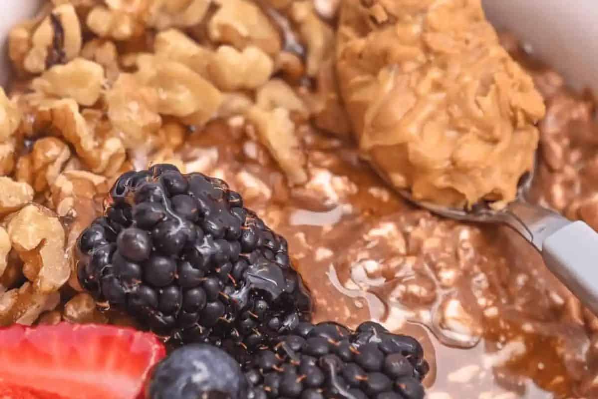 A close-up of a bowl containing oatmeal topped with blackberries, sliced strawberry, blueberries, walnuts, and a spoonful of peanut butter—an inviting sweet and savory option perfect for Valentine’s Day breakfast or creative brunch recipes.