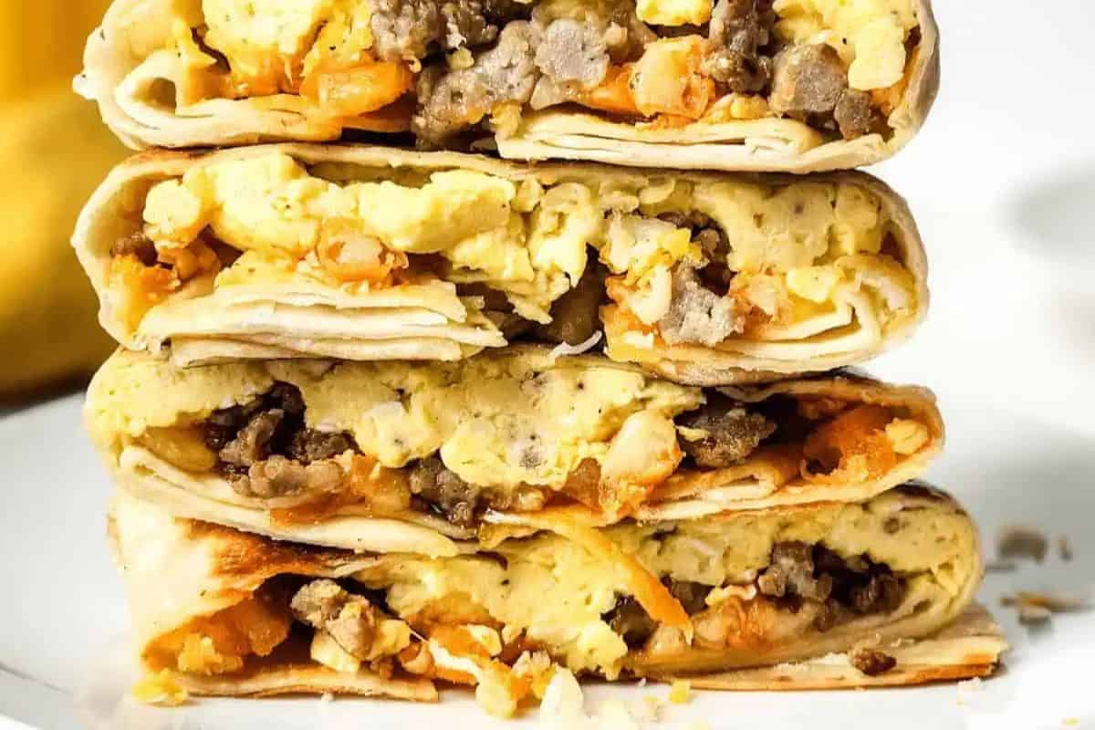A close-up of four stacked breakfast burritos cut in half, showing scrambled eggs, sausage, and cheese inside grilled tortillas—a perfect addition to your list of sweet and savory brunch recipes.