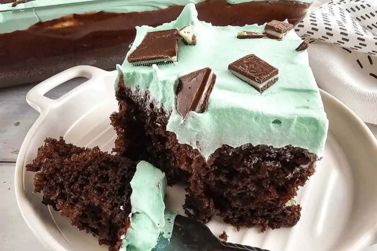 A cute slice of chocolate cake with mint frosting, adorned with mint chocolate pieces, sits invitingly on a plate—perfect for indulging in festive sweets this St. Patrick’s Day.