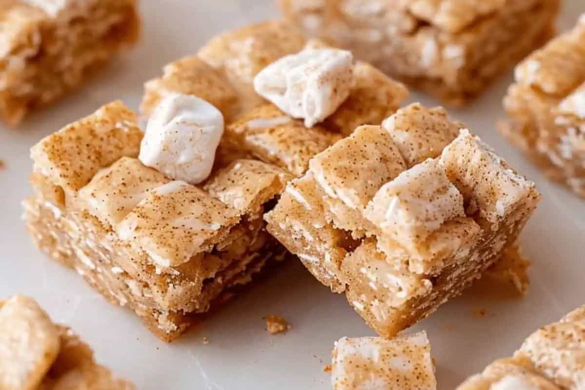 Close-up of cinnamon toast crunch bars topped with marshmallows and dusted with cinnamon on a white surface, these delicious treats bring comfort in every bite.