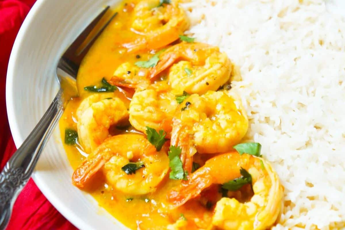 Savor the delightful shrimp curry with herbs, offering restaurant-quality taste, presented alongside a bed of fluffy white rice and a fork.
